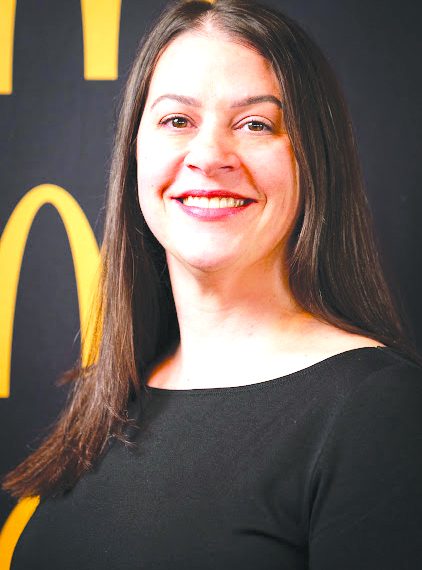 A smiling woman with long dark hair poses for a professional portrait against a black and gold background.