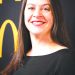 A smiling woman with long dark hair poses for a professional portrait against a black and gold background.
