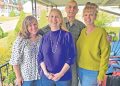 Four family members stand together smiling on a covered porch during a family gathering.