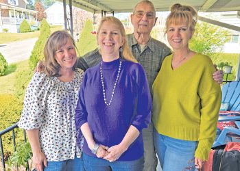 Four family members stand together smiling on a covered porch during a family gathering.