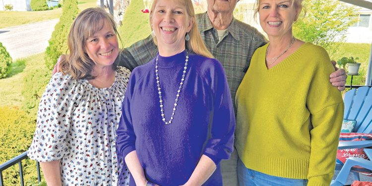 Four family members stand together smiling on a covered porch during a family gathering.