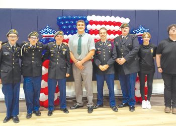 Students and JROTC cadets pose in front of an American flag balloon display during a military recognition ceremony.