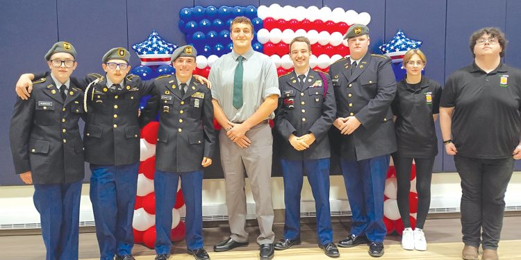 Students and JROTC cadets pose in front of an American flag balloon display during a military recognition ceremony.