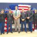 Students and JROTC cadets pose in front of an American flag balloon display during a military recognition ceremony.