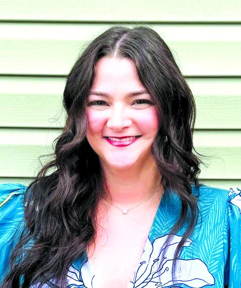 A smiling woman with long dark hair poses in front of a light green wall wearing a blue floral top.