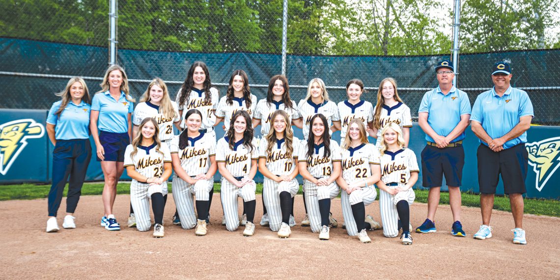 The Carmichaels Lady Mikes softball team and coaches pose together on the softball field for a team photo.