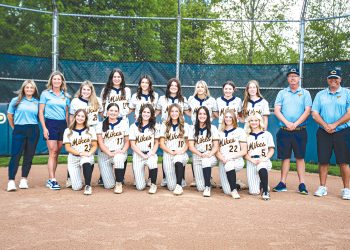 The Carmichaels Lady Mikes softball team and coaches pose together on the softball field for a team photo.