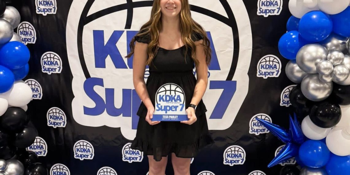 A young woman holds a KDKA Super 7 award while posing in front of an event backdrop and balloon display.