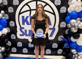 A young woman holds a KDKA Super 7 award while posing in front of an event backdrop and balloon display.