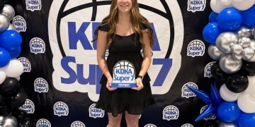 A young woman holds a KDKA Super 7 award while posing in front of an event backdrop and balloon display.