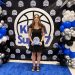 A young woman holds a KDKA Super 7 award while posing in front of an event backdrop and balloon display.