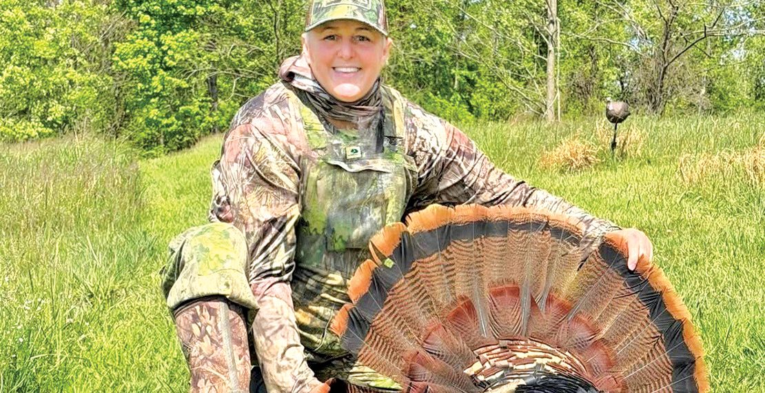 Tammy Hardy posing with turkey in woods.