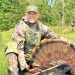 Tammy Hardy posing with turkey in woods.
