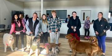 Participants pose with their dogs inside a community center during a community pet walk event.
