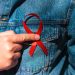 Man wearing Denim Jacket holding a red AIDS awareness ribbon on his chest.