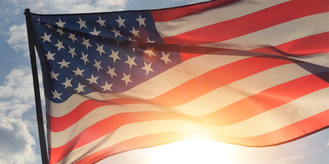 An American flag waves in the sunlight against a partly cloudy sky.