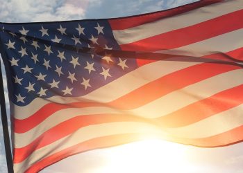 An American flag waves in the sunlight against a partly cloudy sky.