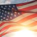 An American flag waves in the sunlight against a partly cloudy sky.