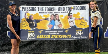 Nikki Gasti Onderko and Bailey Barnyak hold a banner celebrating the Carmichaels High School career strikeout record passing from mother to daughter.