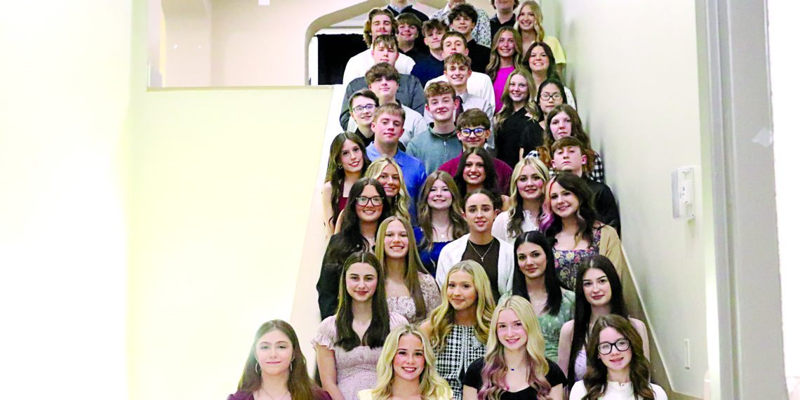 A group of National Honor Society students poses on a staircase inside a school building for a formal group photo.