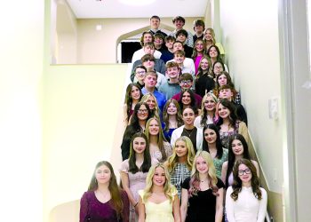 A group of National Honor Society students poses on a staircase inside a school building for a formal group photo.