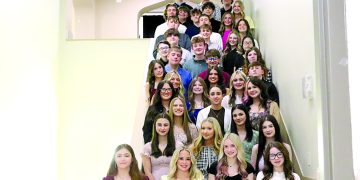A group of National Honor Society students poses on a staircase inside a school building for a formal group photo.