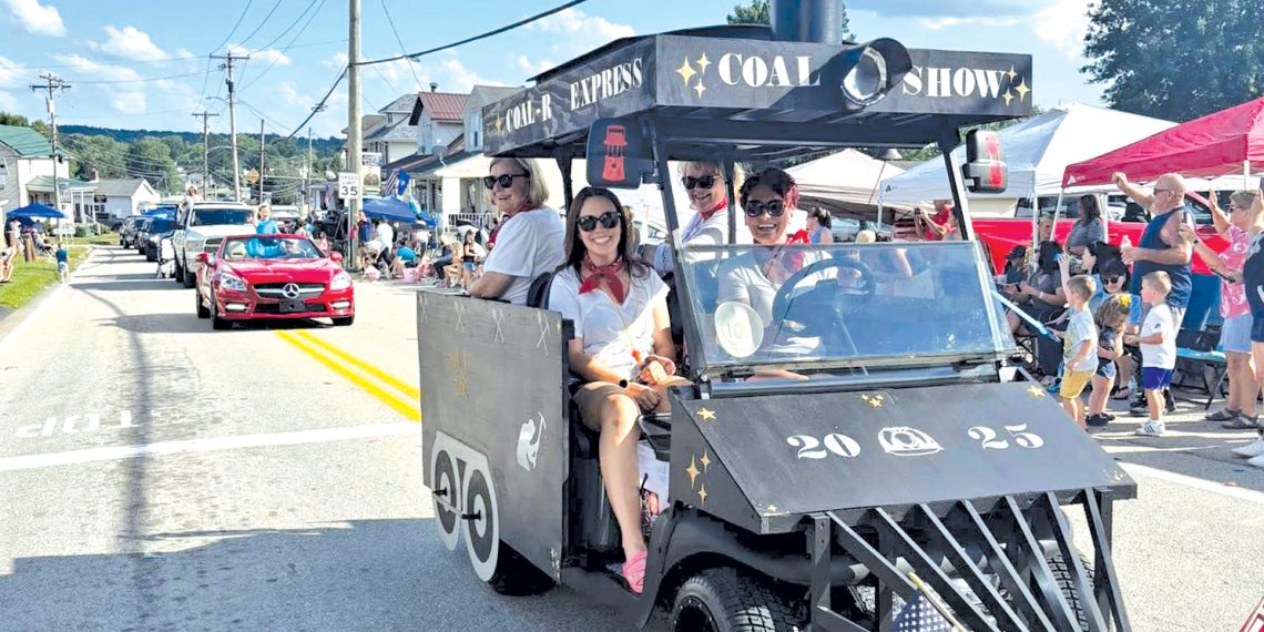 A train themed parade vehicle travels through the Pennsylvania Bituminous King Coal Show parade as spectators watch from the roadside.