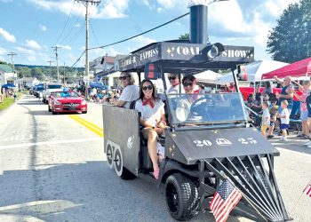 A train themed parade vehicle travels through the Pennsylvania Bituminous King Coal Show parade as spectators watch from the roadside.