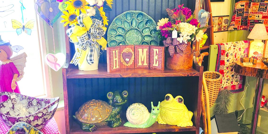 A rustic display inside a country gift shop features floral arrangements, ceramic frogs, decorative signs, and handcrafted home decor.