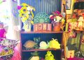 A rustic display inside a country gift shop features floral arrangements, ceramic frogs, decorative signs, and handcrafted home decor.
