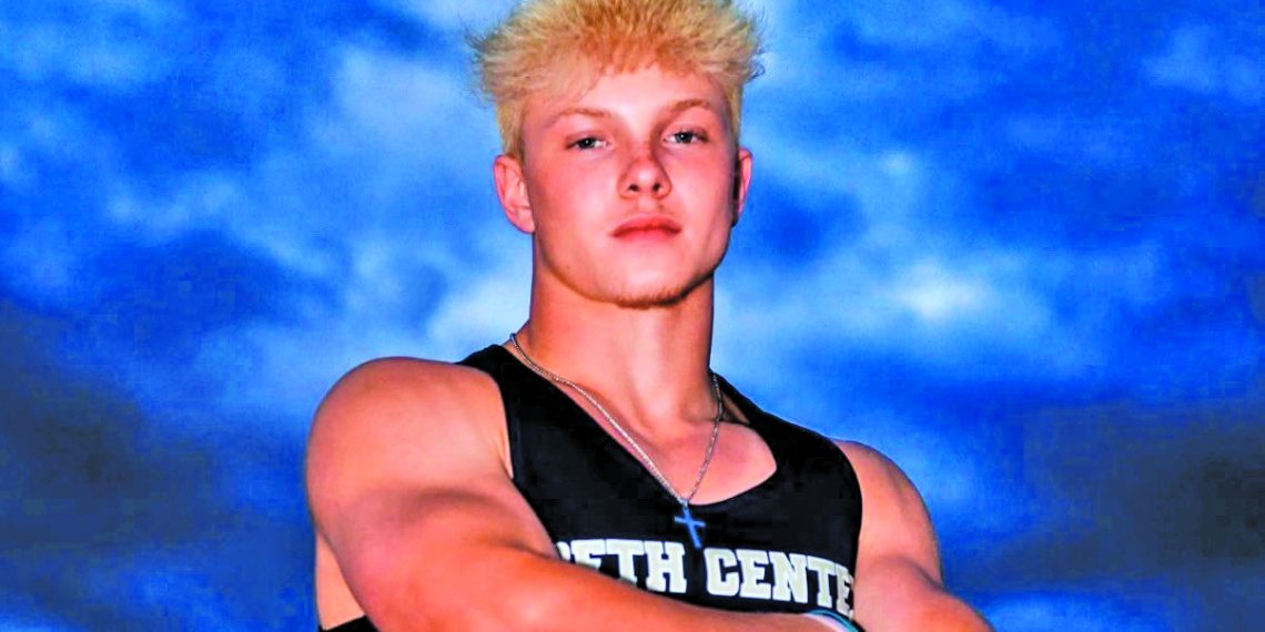 State champion sprinter Deakyn DeHoet poses in his Beth Center track and field uniform with his arms crossed beneath a dramatic evening sky.