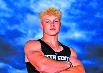 State champion sprinter Deakyn DeHoet poses in his Beth Center track and field uniform with his arms crossed beneath a dramatic evening sky.