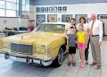 A family stands beside a vintage yellow Mercury convertible inside a Ford dealership showroom.