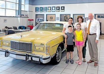 A family stands beside a vintage yellow Mercury convertible inside a Ford dealership showroom.