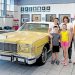 A family stands beside a vintage yellow Mercury convertible inside a Ford dealership showroom.