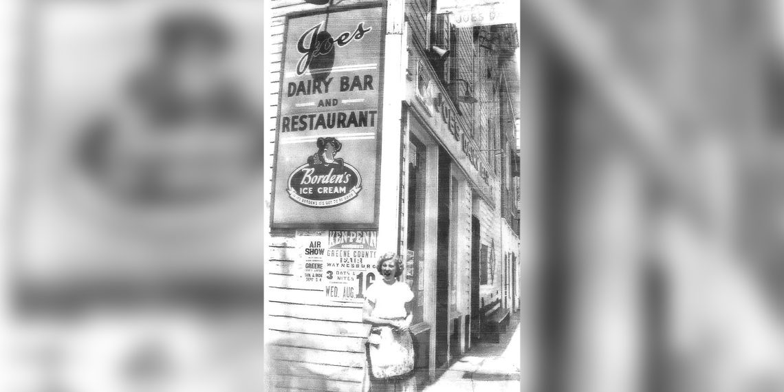 A historic black and white photo shows the exterior of Joe's Dairy Bar and Restaurant in Waynesburg with a woman standing on the sidewalk beneath the iconic sign.
