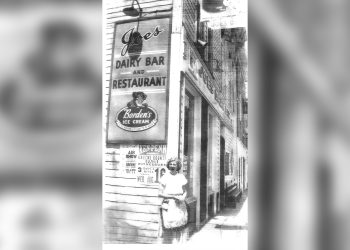A historic black and white photo shows the exterior of Joe's Dairy Bar and Restaurant in Waynesburg with a woman standing on the sidewalk beneath the iconic sign.