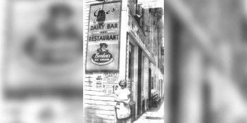 A historic black and white photo shows the exterior of Joe's Dairy Bar and Restaurant in Waynesburg with a woman standing on the sidewalk beneath the iconic sign.