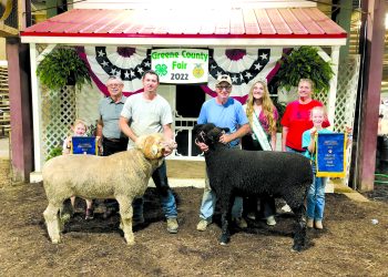Exhibitors, family members, and fair royalty pose with a champion ram and champion sheep while children display championship banners at the Greene County Fair.