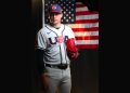 Mason Miller stands in his Team USA baseball uniform holding a red glove in front of an American flag backdrop.