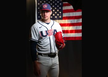 Mason Miller stands in his Team USA baseball uniform holding a red glove in front of an American flag backdrop.