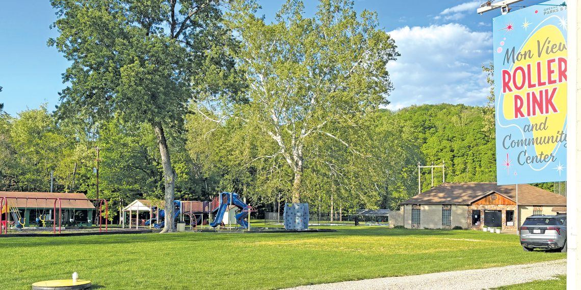 A scenic view of Mon View Park in Greensboro features playgrounds, open grassy areas, large trees, and the Mon View Roller Rink and Community Center sign.