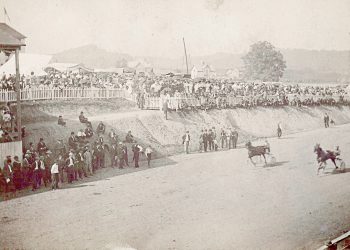 A historic photograph shows spectators watching a harness horse race on a dirt track at an early county fair.