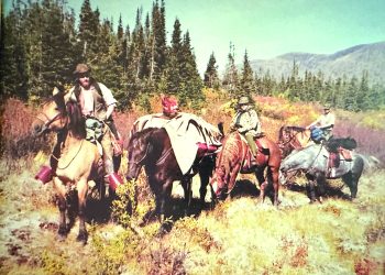 A group of hunters on horseback gathers in a mountain meadow with pack horses carrying harvested game during a backcountry hunt.