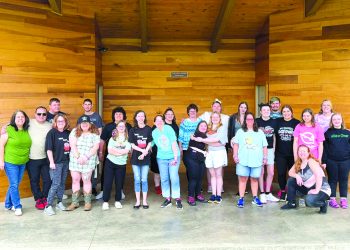 Special Olympics participants, volunteers, and supporters pose together on an outdoor stage during a community picnic.