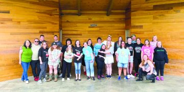 Special Olympics participants, volunteers, and supporters pose together on an outdoor stage during a community picnic.