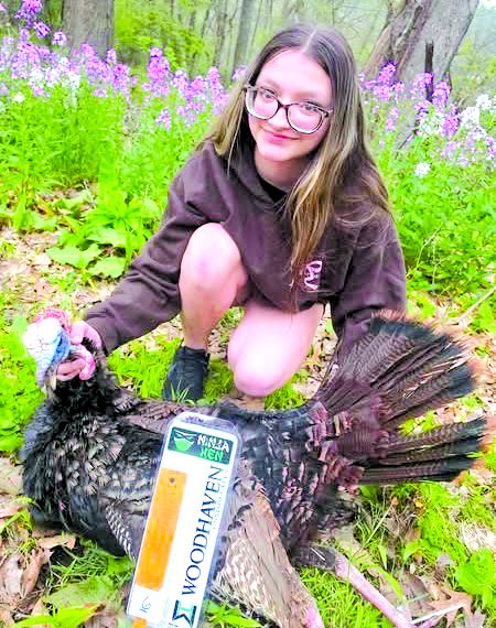 A young hunter poses with a harvested wild turkey in a wooded area during spring turkey season.