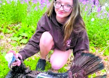 A young hunter poses with a harvested wild turkey in a wooded area during spring turkey season.
