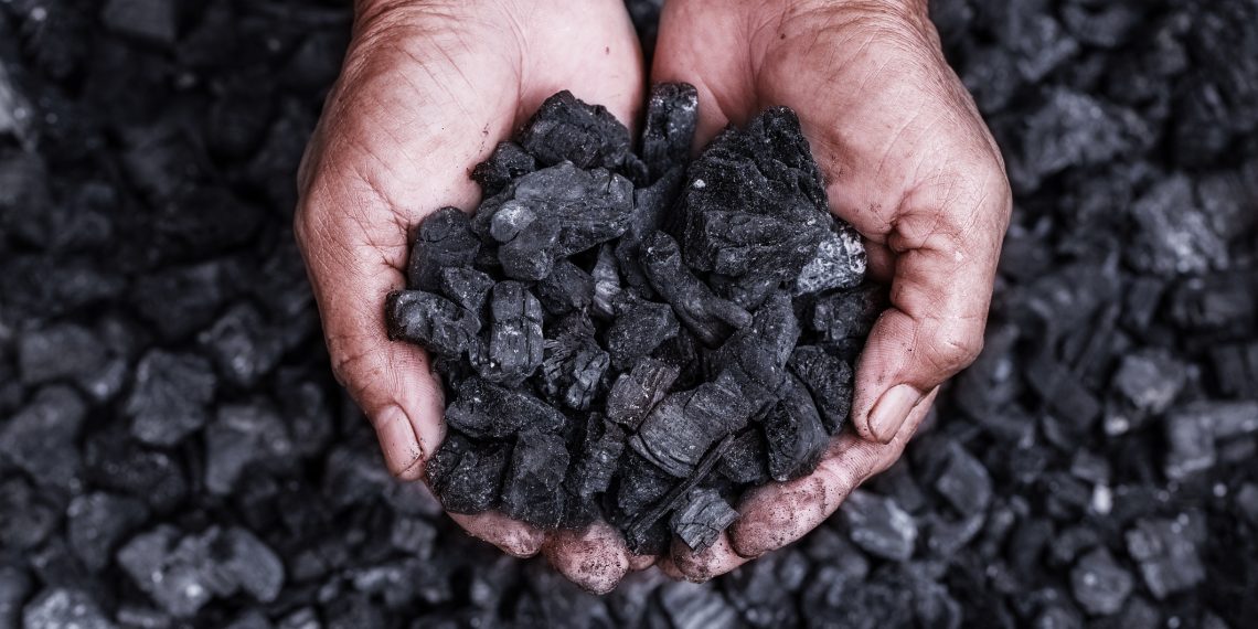 A pair of hands holds a pile of coal with a background of loose coal pieces.