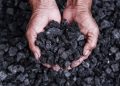 A pair of hands holds a pile of coal with a background of loose coal pieces.